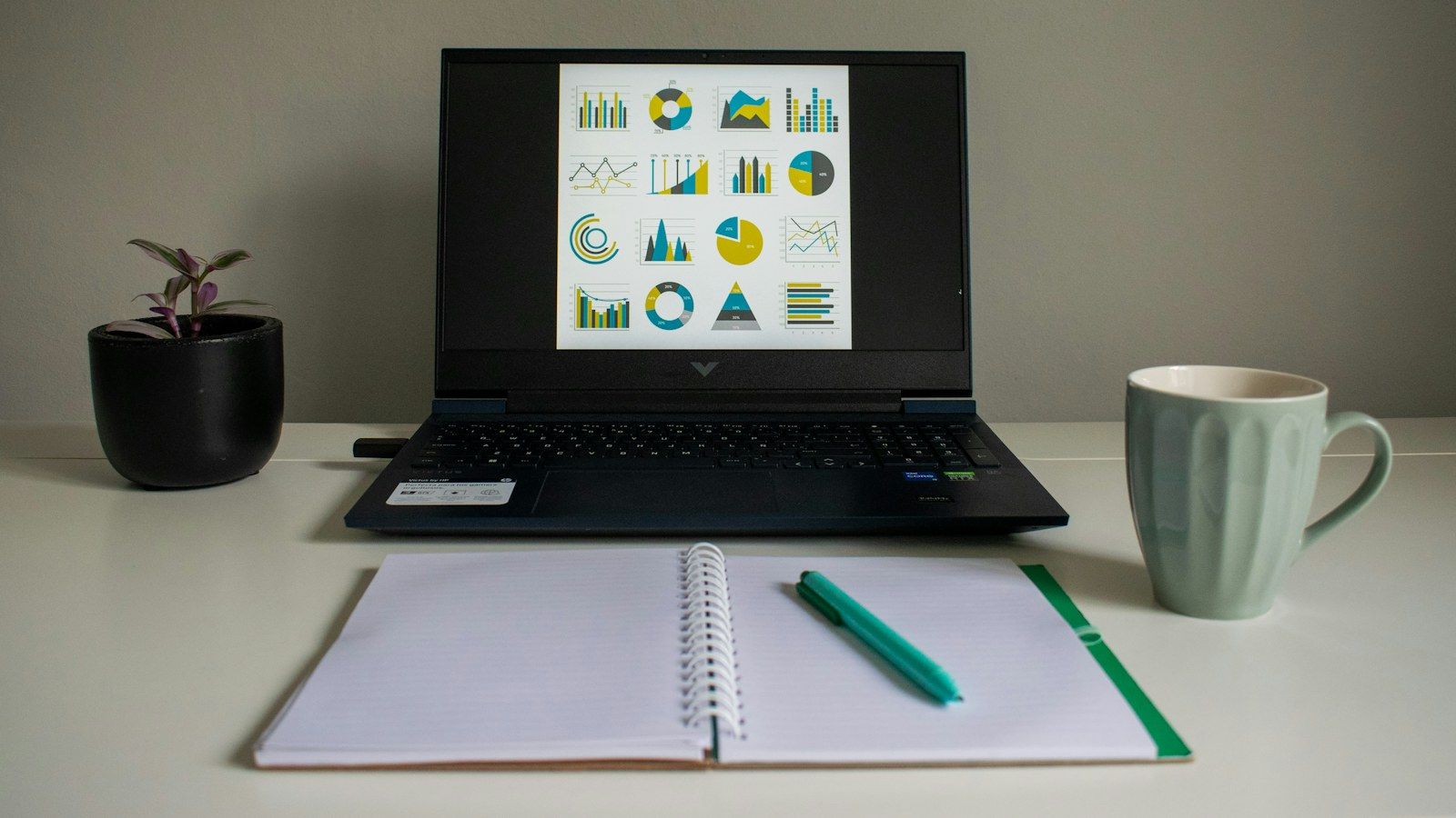 Laptop mit Diagrammen und Analysen neben einem aufgeschlagenen Notizbuch